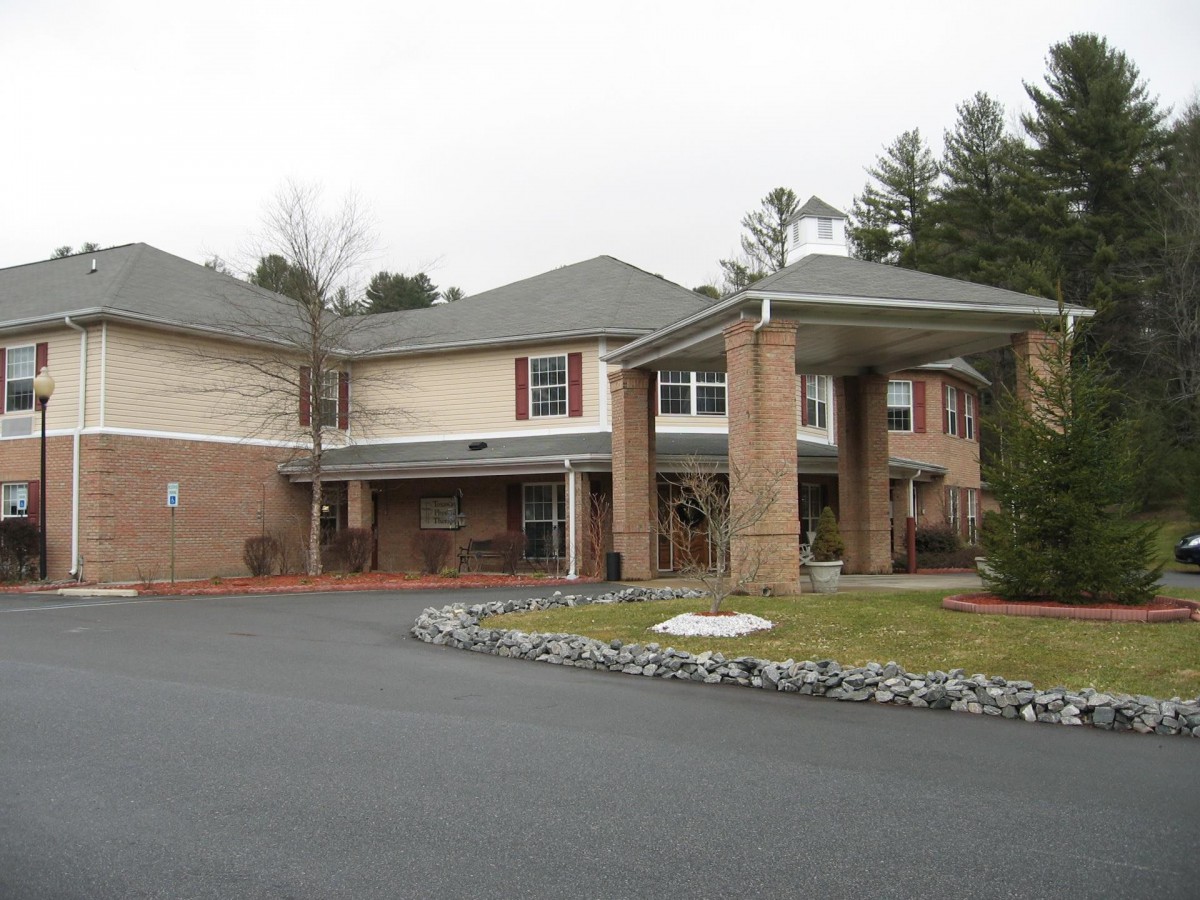 A two-story brick building with a covered entrance and surrounding greenery.