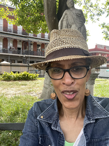 A cheerful woman enjoying a sunny day in the park, wearing a stylish hat and glasses.