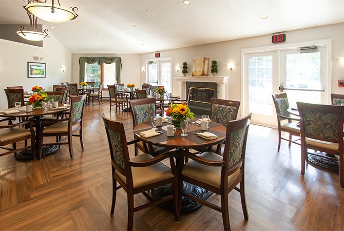 A well-decorated dining room with neatly arranged tables and chairs, featuring a wooden floor and floral centerpieces.