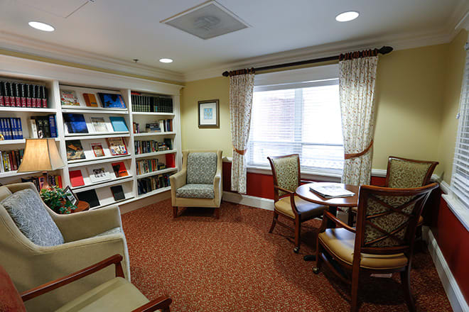 A cozy reading area with a bookshelf, chairs, and a table by the window.