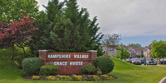 Entrance sign for Hampshire Village and Grace House surrounded by trees and greenery.
