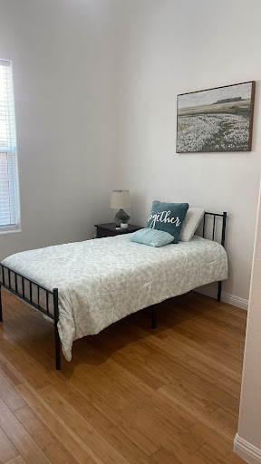 A cozy and minimalist bedroom featuring a single bed with light bedding and a bedside lamp.