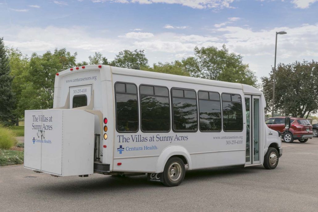 A white shuttle bus parked outdoors near some trees.