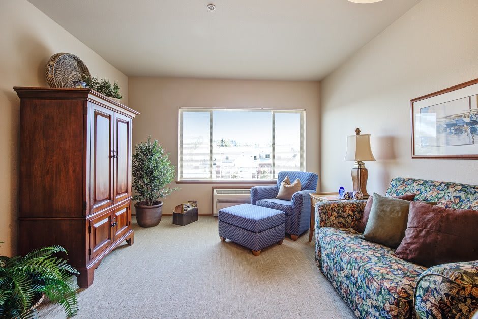 A cozy living room with a sofa, armchair, and large window letting in natural light.