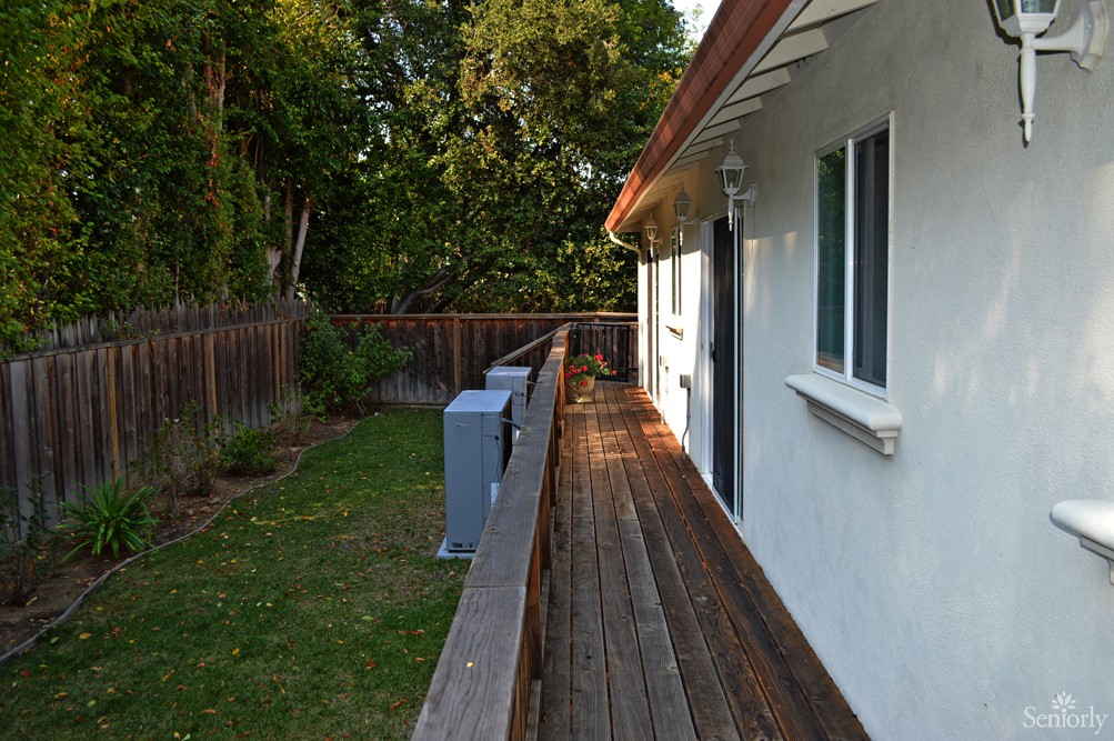A backyard featuring a wooden deck alongside a house, bordered by a fence and surrounded by trees.