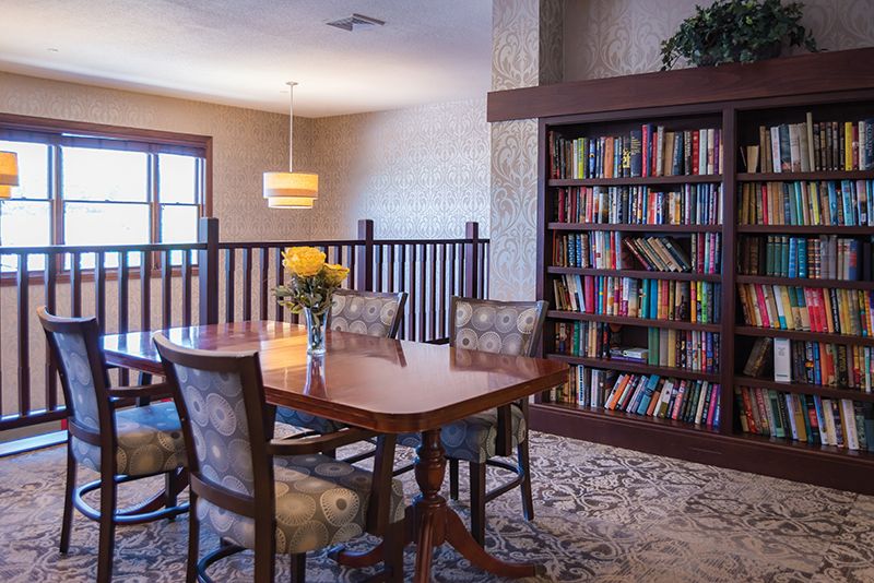 A cozy dining area featuring a wooden table, upholstered chairs, and a large bookshelf filled with books.