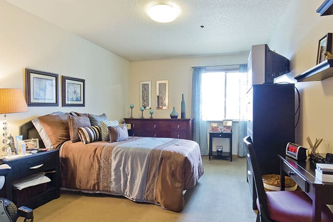 A cozy bedroom with neatly arranged furniture and a window letting in natural light.