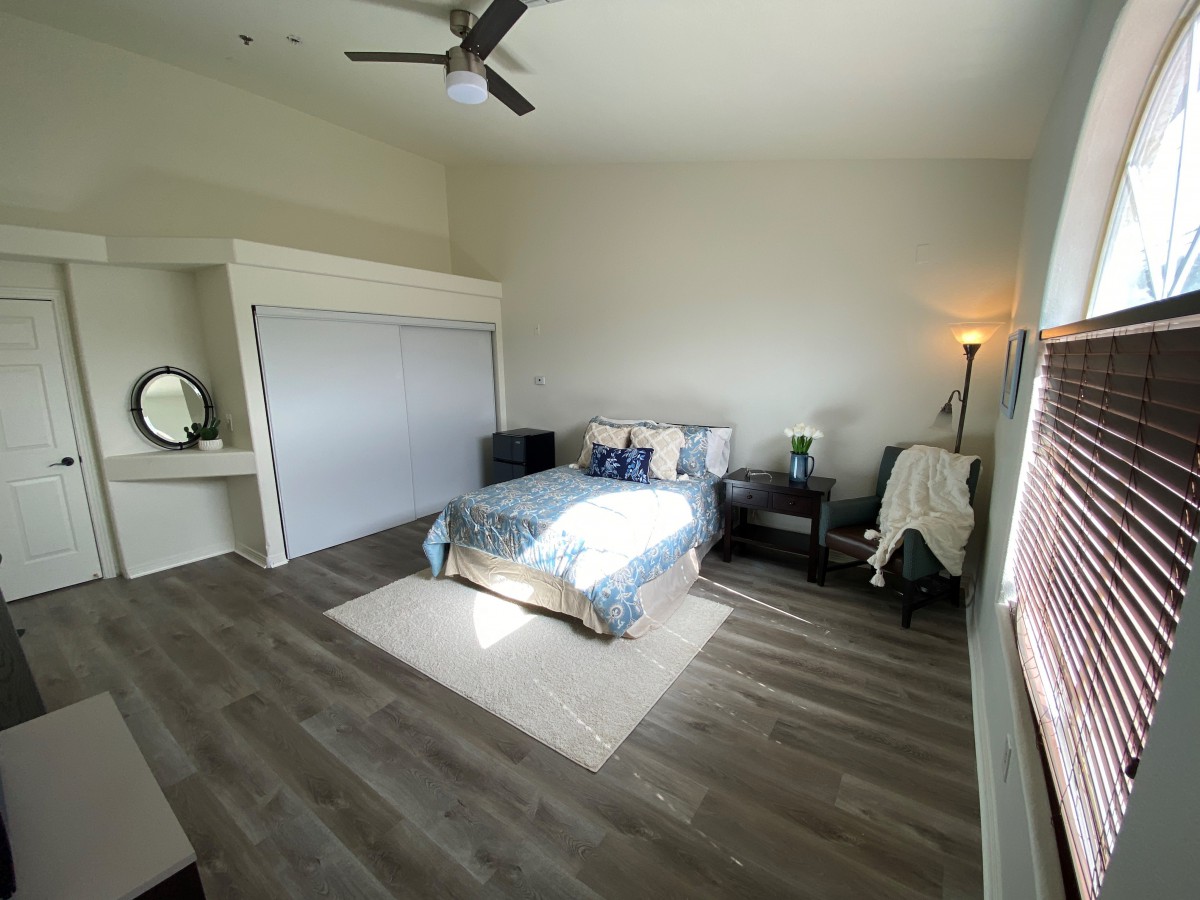 A spacious and minimalist bedroom with modern decor, featuring a double bed, wooden flooring, and ample natural light.