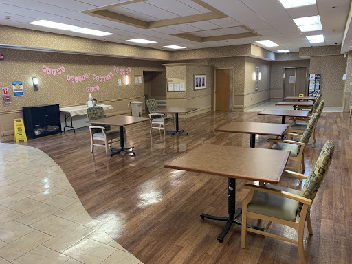 A spacious and empty dining hall featuring wooden floors, tables, and chairs, ready for an event or gathering.