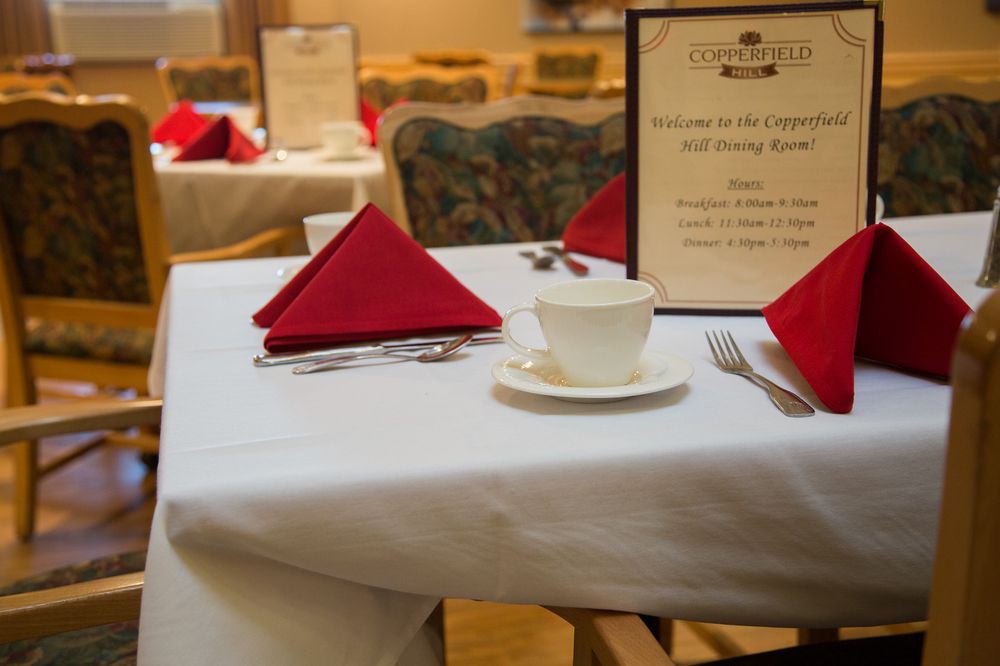 A neatly arranged dining table in a restaurant with a menu, cup, saucer, and red folded napkins.