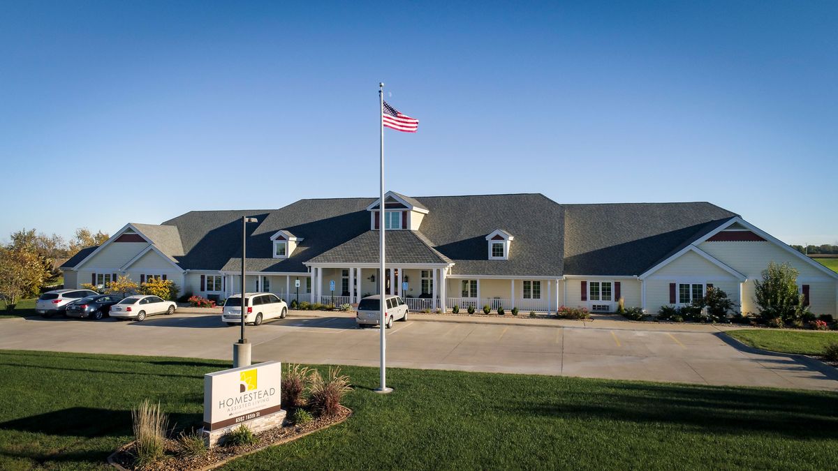 An exterior view of a building with an American flag in front and parked cars in the lot.