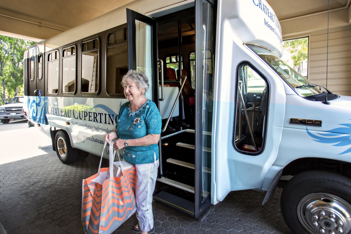 An elderly woman stepping off a bus while holding a shopping bag.