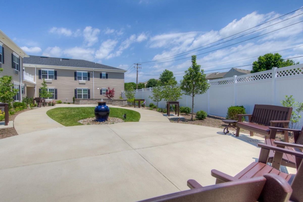 A residential backyard featuring a garden area with benches and young trees, enclosed by a white fence.