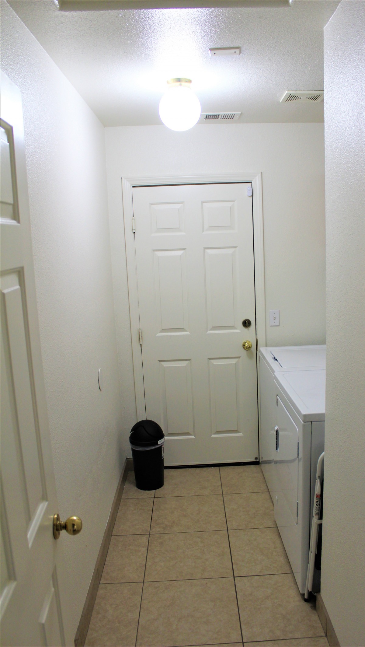 A compact laundry room with a washer, dryer, and a small trash can next to a white door.