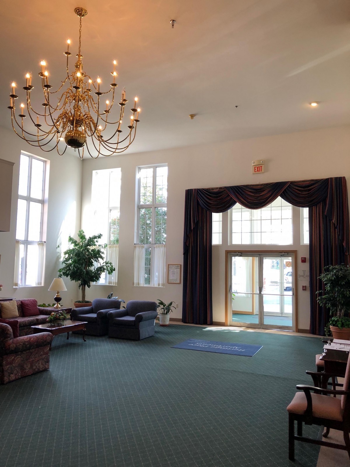 A spacious lobby with a grand chandelier, ample seating, and natural light streaming through large windows.