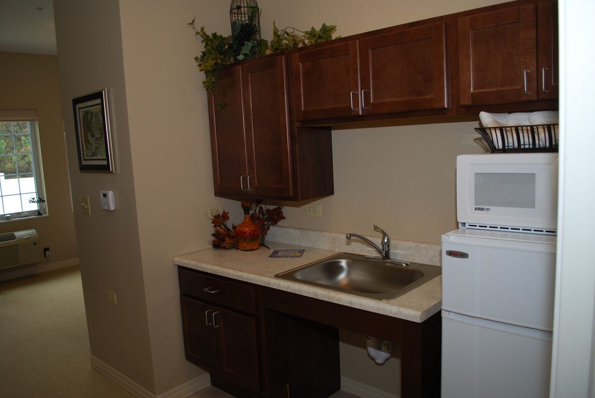 A small kitchen area with wooden cabinets, a sink, and appliances including a refrigerator and microwave.