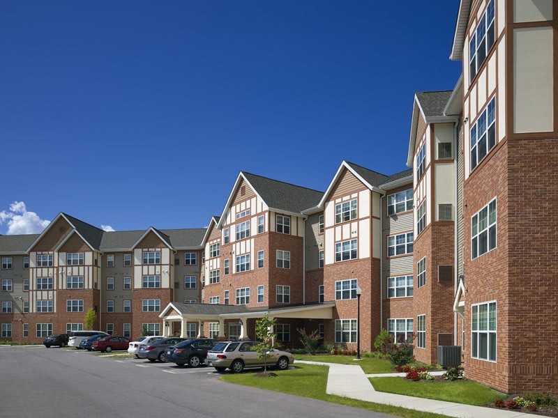 A multi-story residential apartment building with a parking area in front under a clear blue sky.