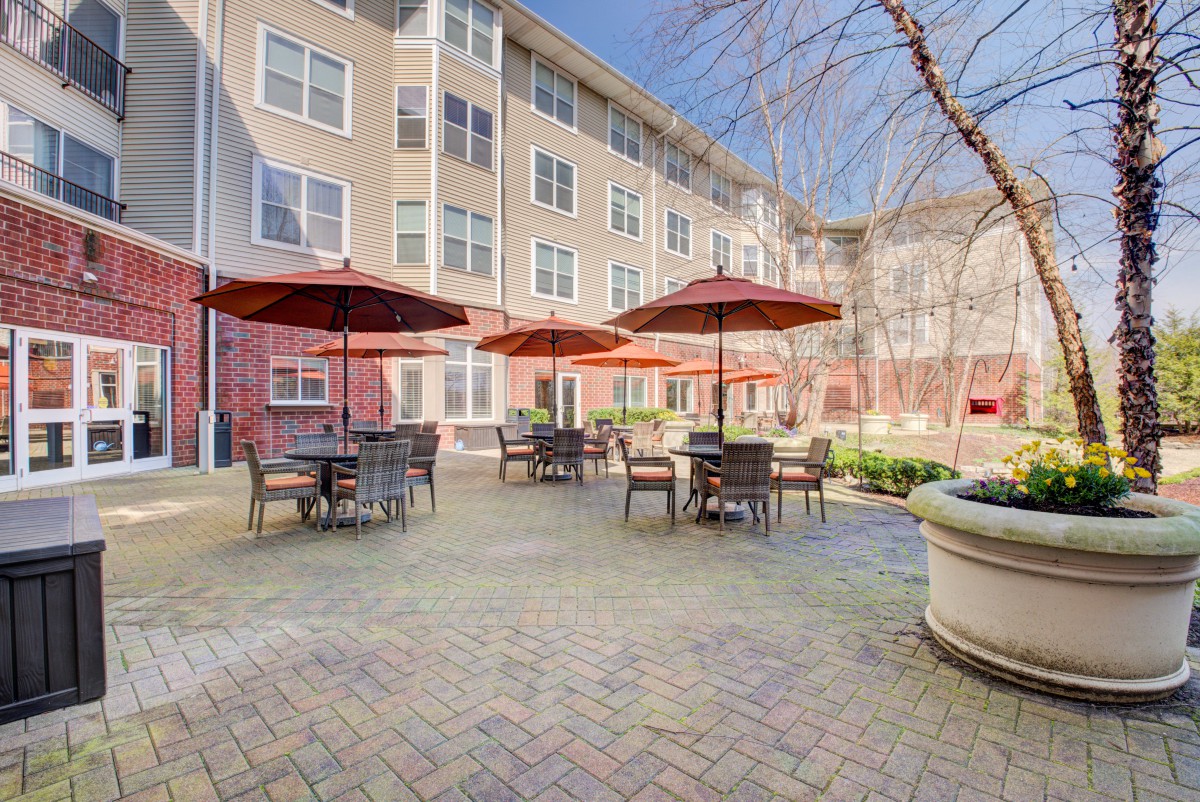 A cozy outdoor patio area with tables, chairs, and umbrellas in an apartment complex courtyard.