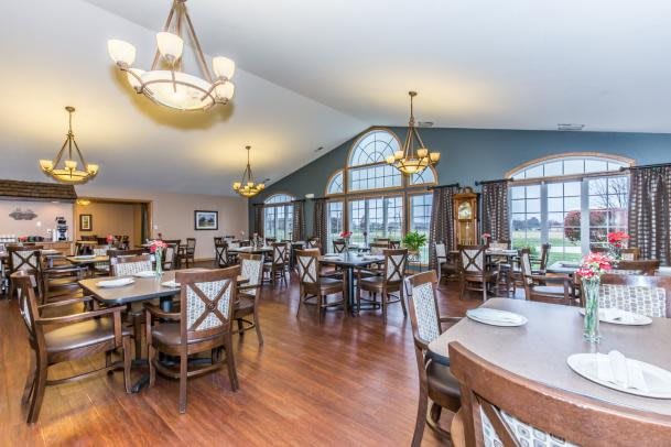 A spacious and elegantly decorated dining area with wooden floors, featuring multiple tables and chairs, large windows, and chandeliers.