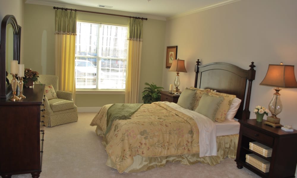 A cozy and elegantly decorated bedroom featuring a large bed with floral bedding, a window with curtains, and a comfortable armchair.