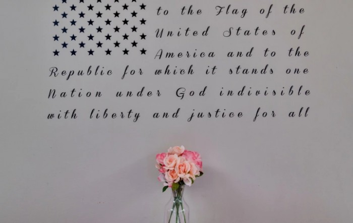 A wall with patriotic text and a vase holding pink flowers in front of it.
