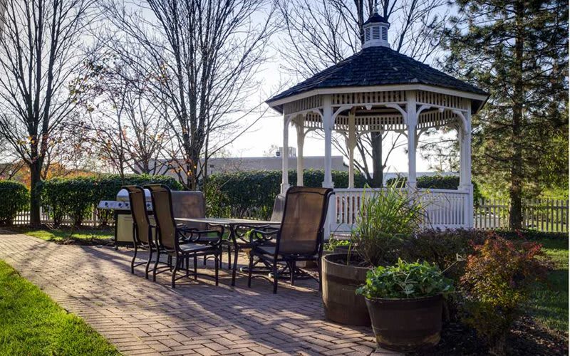 A charming outdoor patio with a gazebo and seating area surrounded by lush plants.