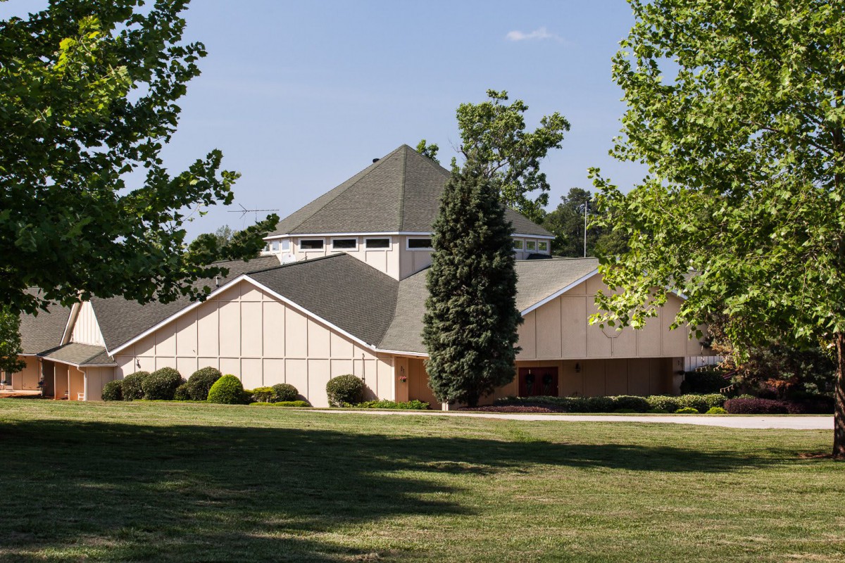 A suburban house surrounded by trees and a well-kept lawn on a sunny day.