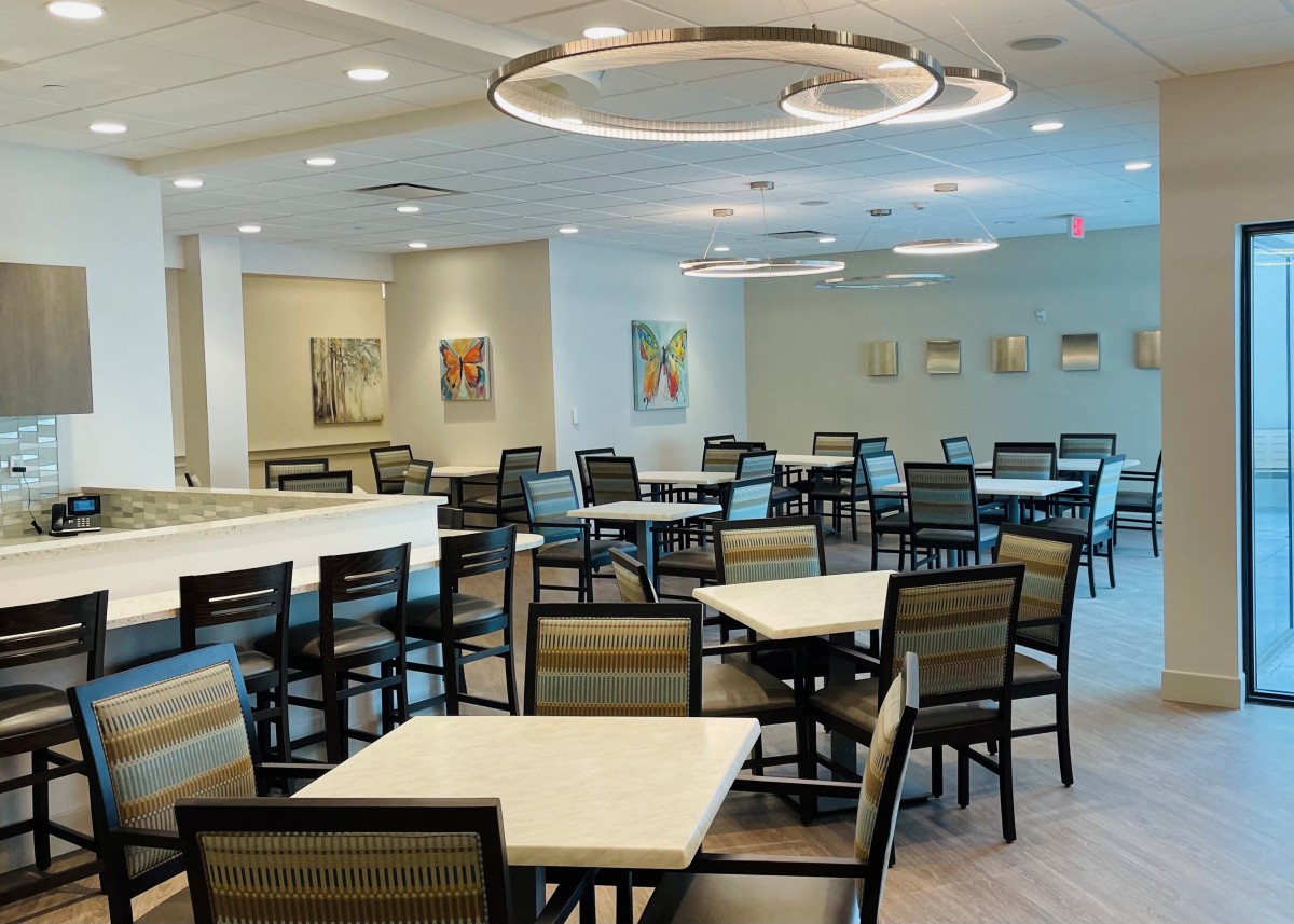 A modern dining area with empty tables and chairs, featuring contemporary lighting and wall art.