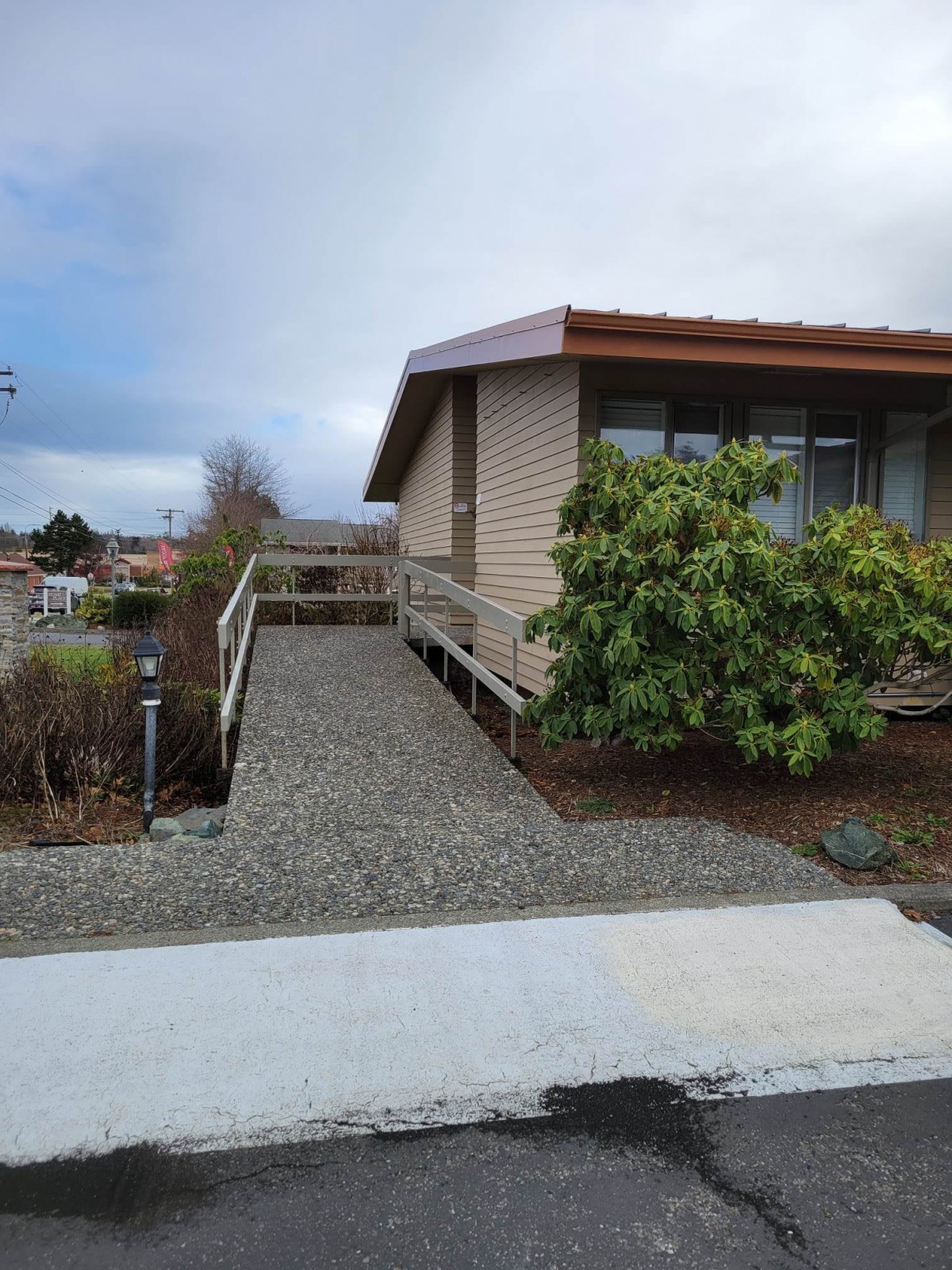 A suburban house with a ramp leading to the entrance, surrounded by landscaping under an overcast sky.