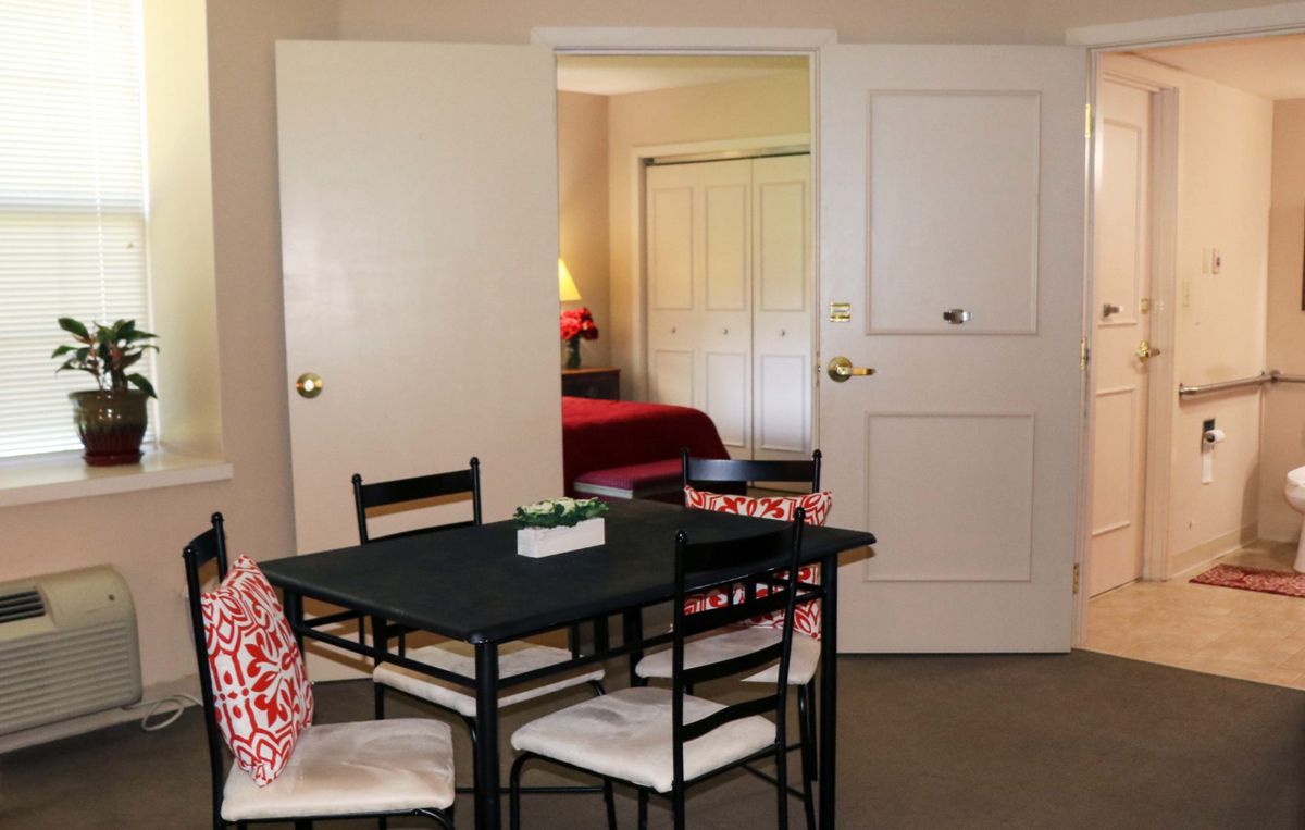 A cozy dining area with a view into the bedroom, featuring a small table and chairs with decorative pillows.