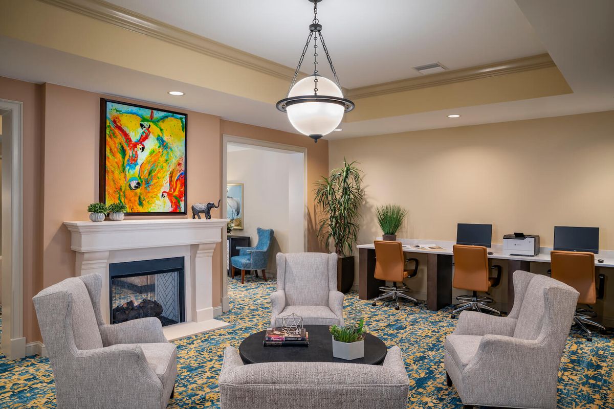 A modern living room with a colorful painting above the fireplace, comfortable seating, and a workspace area.