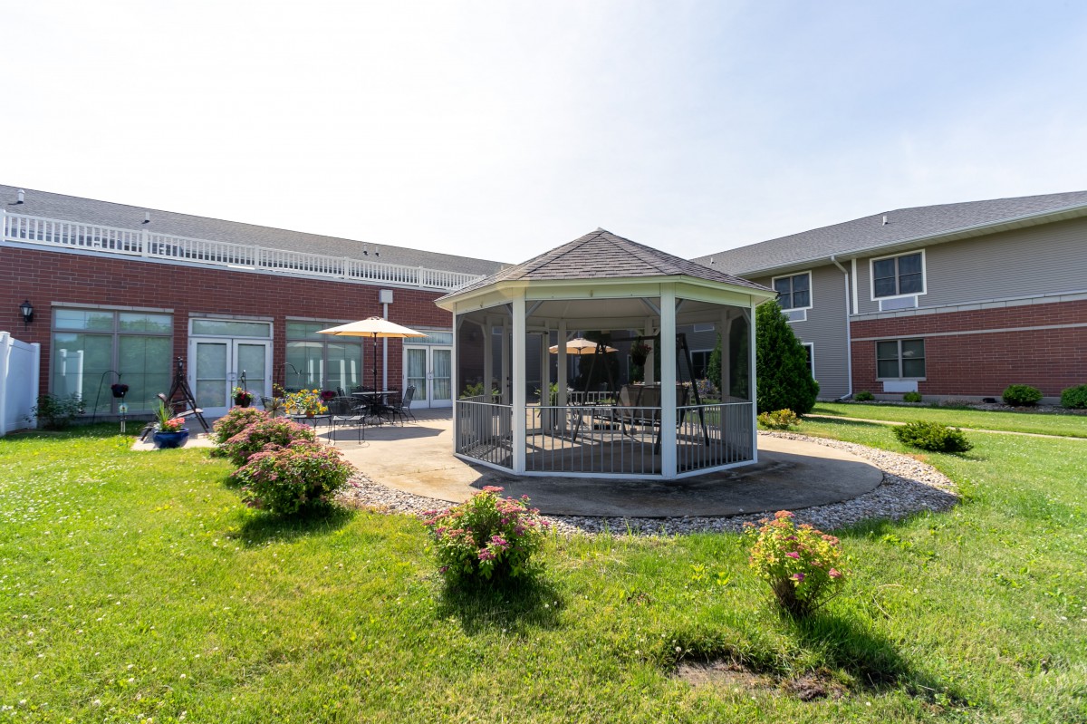 A charming gazebo situated in a landscaped garden area with a surrounding lawn and adjacent building.