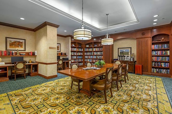 A cozy library reading room with a large wooden table and chairs surrounded by bookshelves.