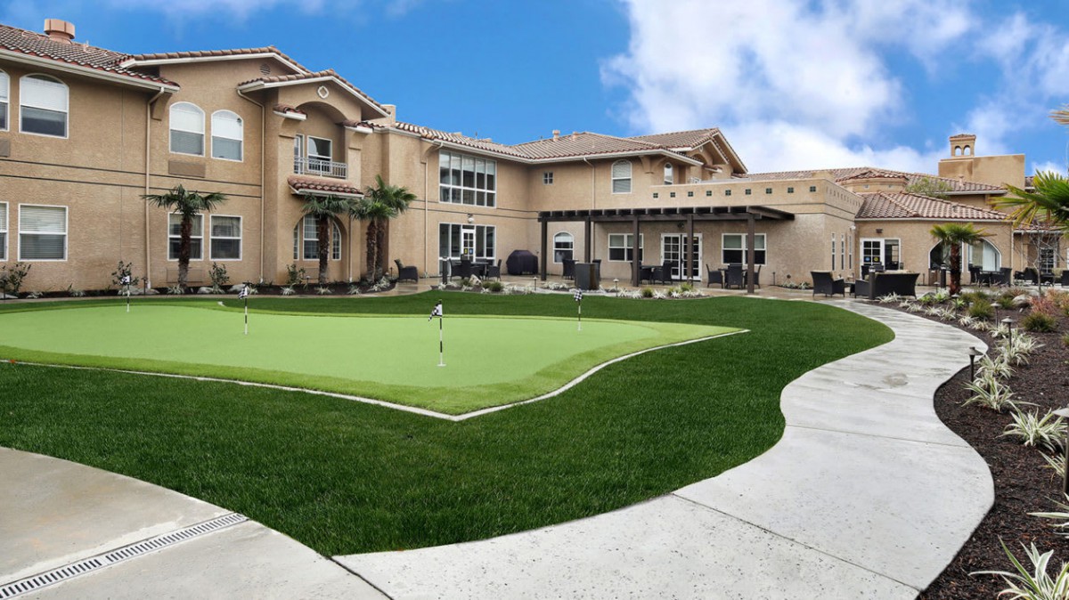 A luxurious mansion with a well-maintained backyard featuring a putting green.