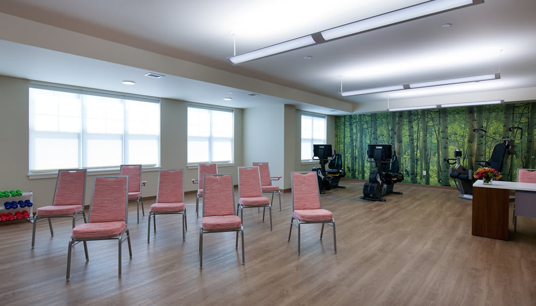 An empty room with arranged chairs, exercise equipment, and large windows.