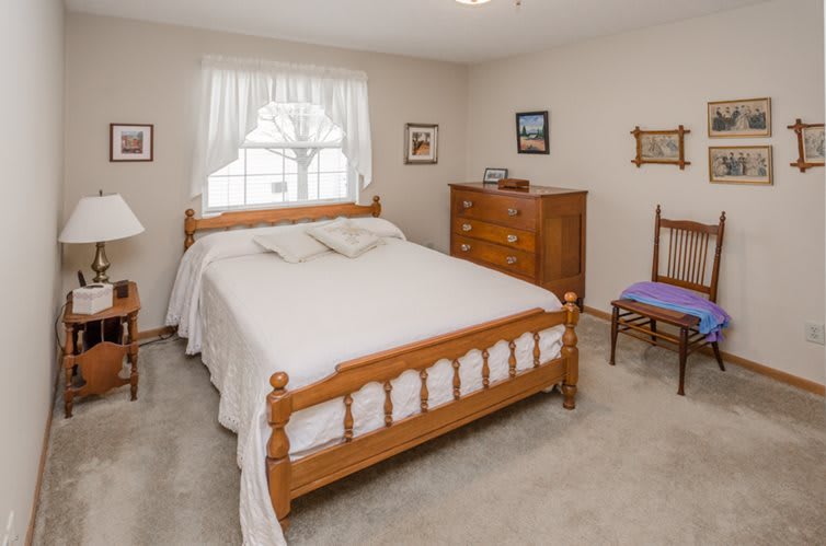 A cozy bedroom featuring a wooden bed, dresser, and chair with soft carpet flooring.
