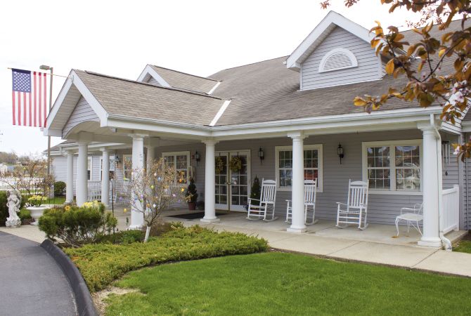 A charming residential house with a porch and rocking chairs, surrounded by well-maintained landscaping.