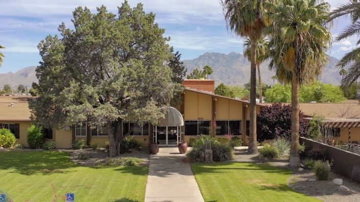 A mid-century building surrounded by greenery with a mountainous backdrop.