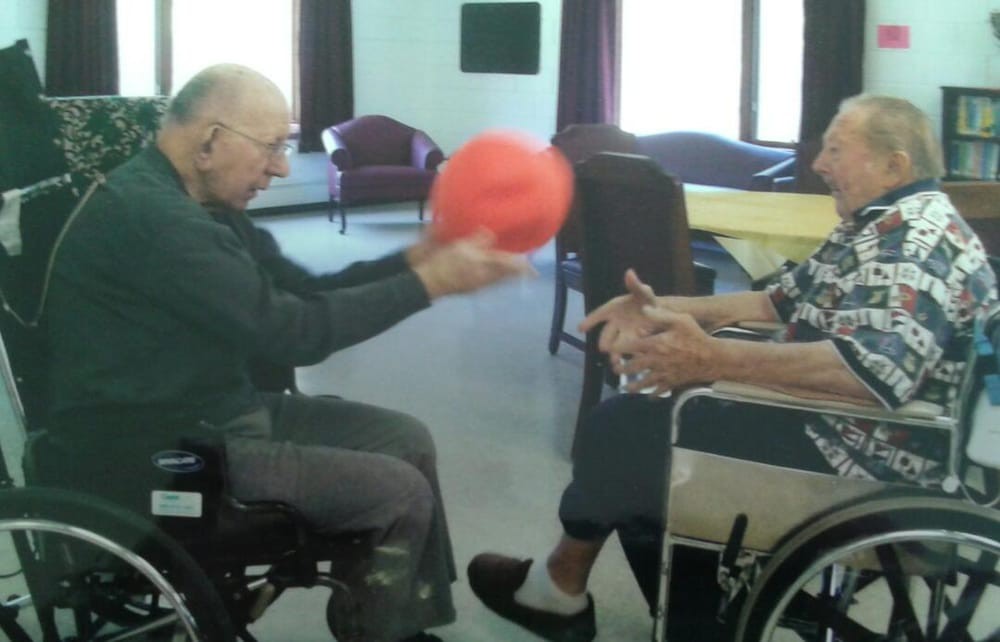 Elderly individuals playing with a ball while seated in wheelchairs indoors.