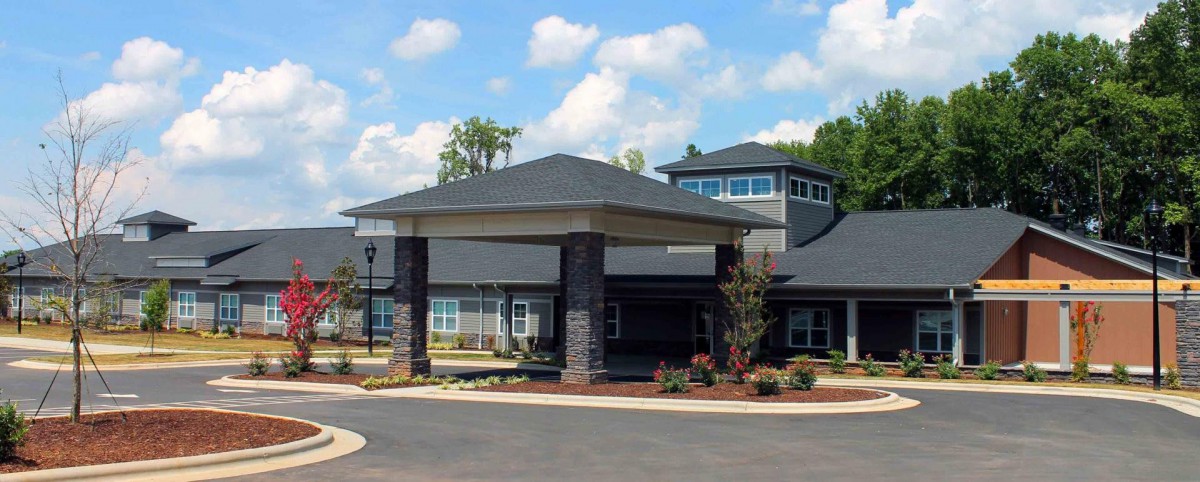 A modern building with a covered entrance and landscaped surroundings under a partly cloudy sky.