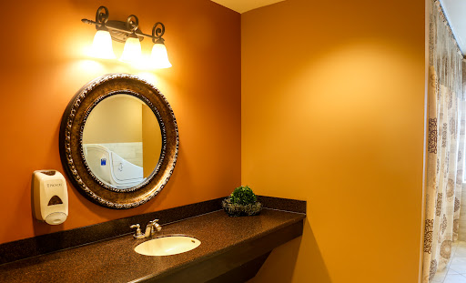 A stylish modern bathroom featuring an orange wall, a round mirror, and elegant lighting.
