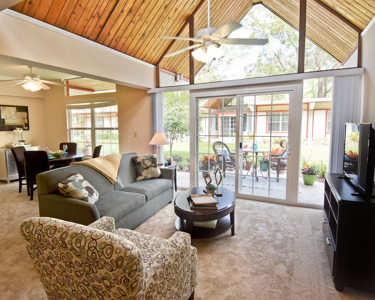 A cozy living room featuring a wooden ceiling and large windows overlooking an outdoor space.