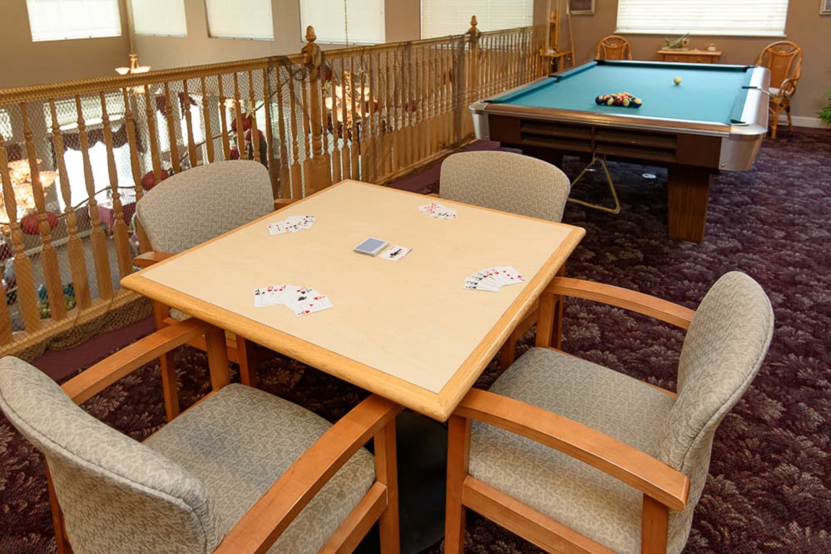 A cozy game room featuring a card table with a deck of cards and a pool table in the background.