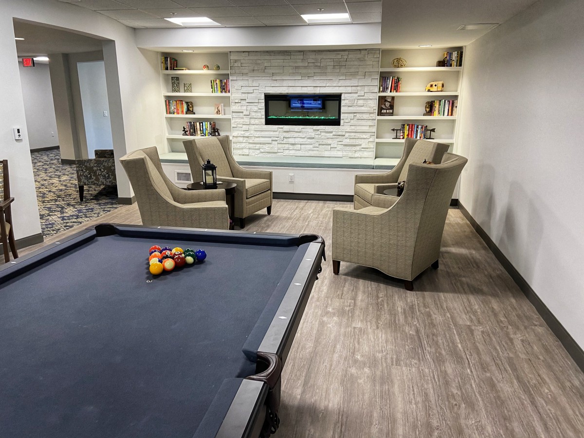 A modern game room featuring a pool table and lounge area with bookshelves and a television.