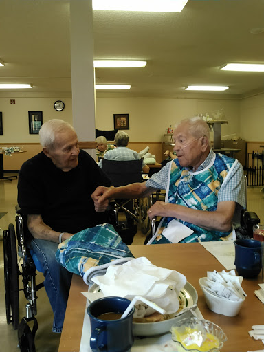 Two elderly individuals engage in a warm conversation at a care facility.