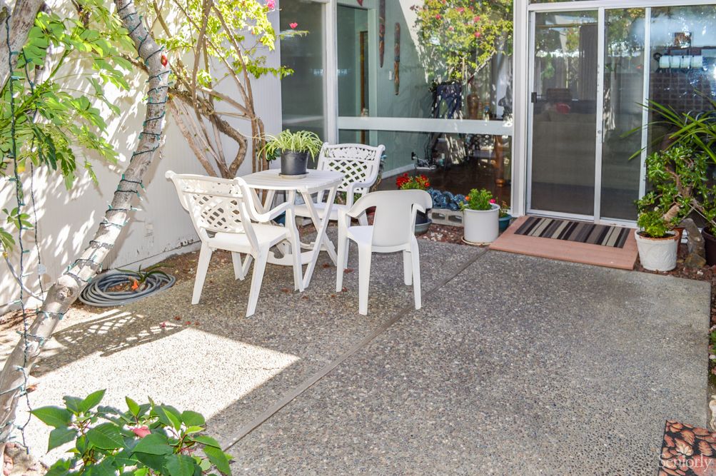 A sunny patio with white outdoor furniture set among greenery.
