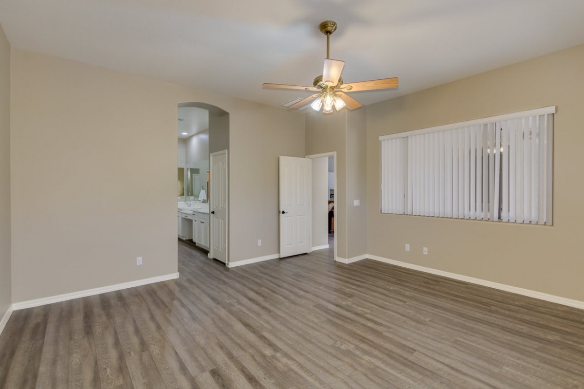 An empty room with hardwood flooring, a ceiling fan, and a doorway leading to another area.