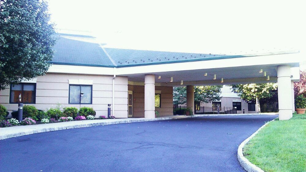 The image depicts the exterior entrance of a building with a covered driveway and columns.