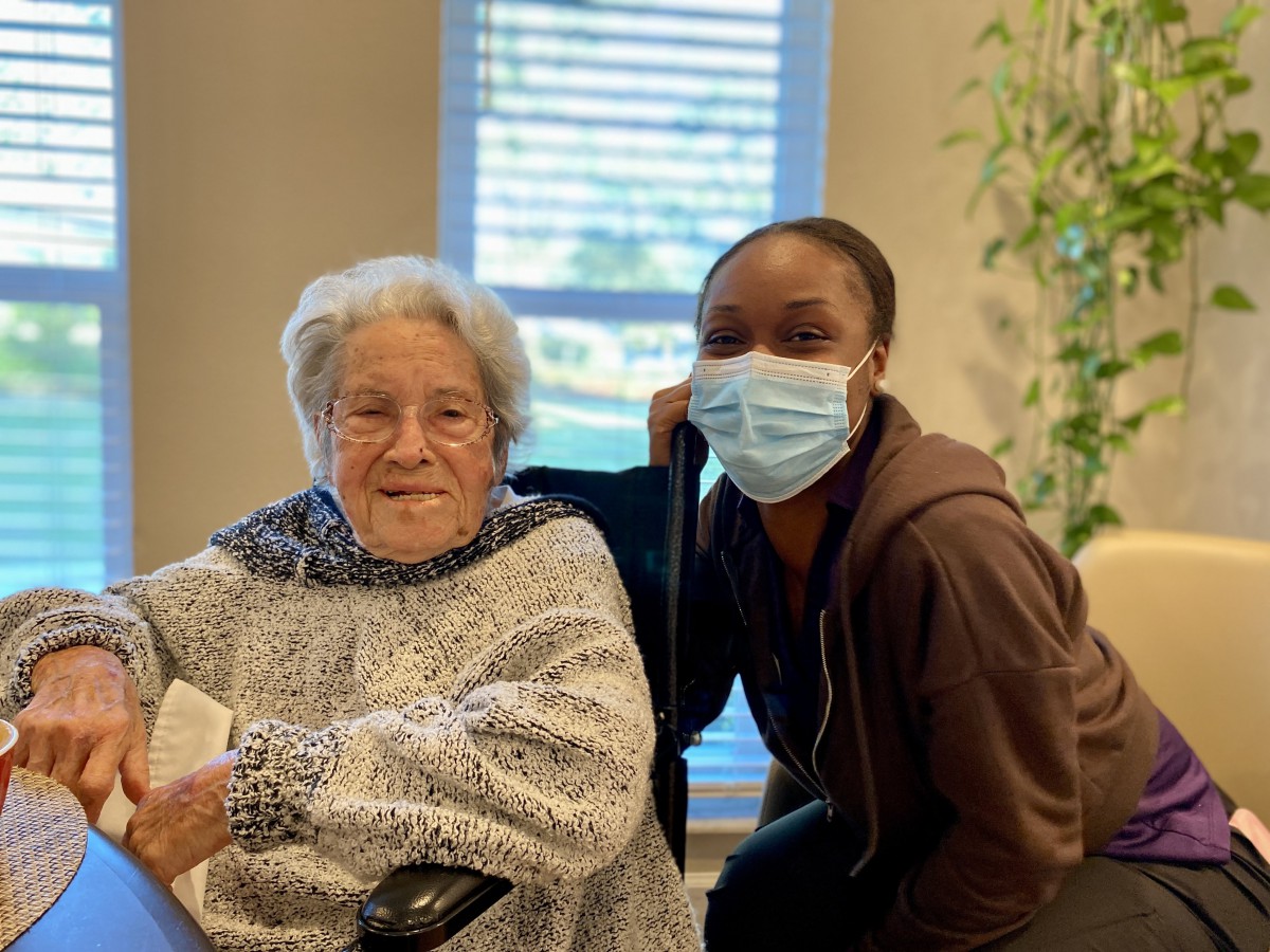 An elderly woman and a healthcare worker smiling together indoors.
