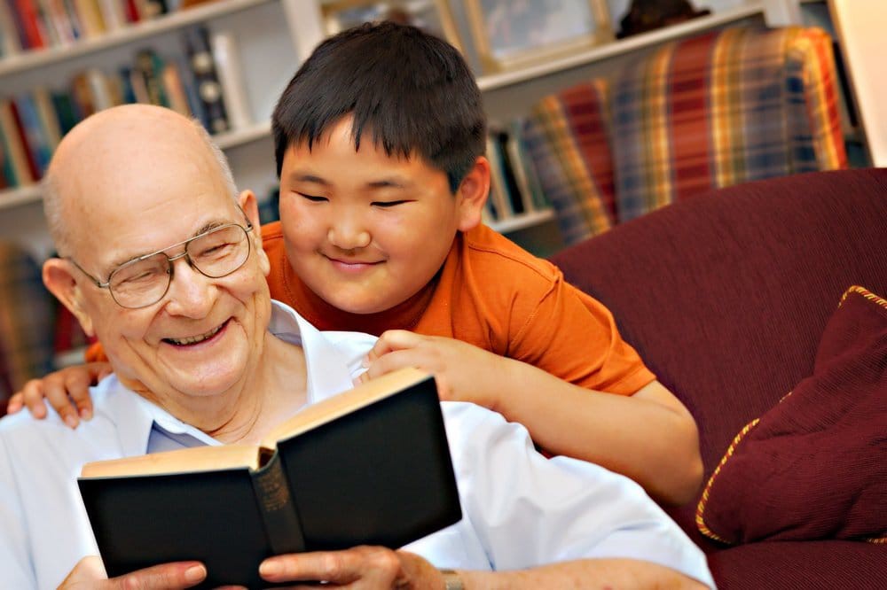 A grandfather and grandson enjoying a book together, sharing a joyful moment at home.